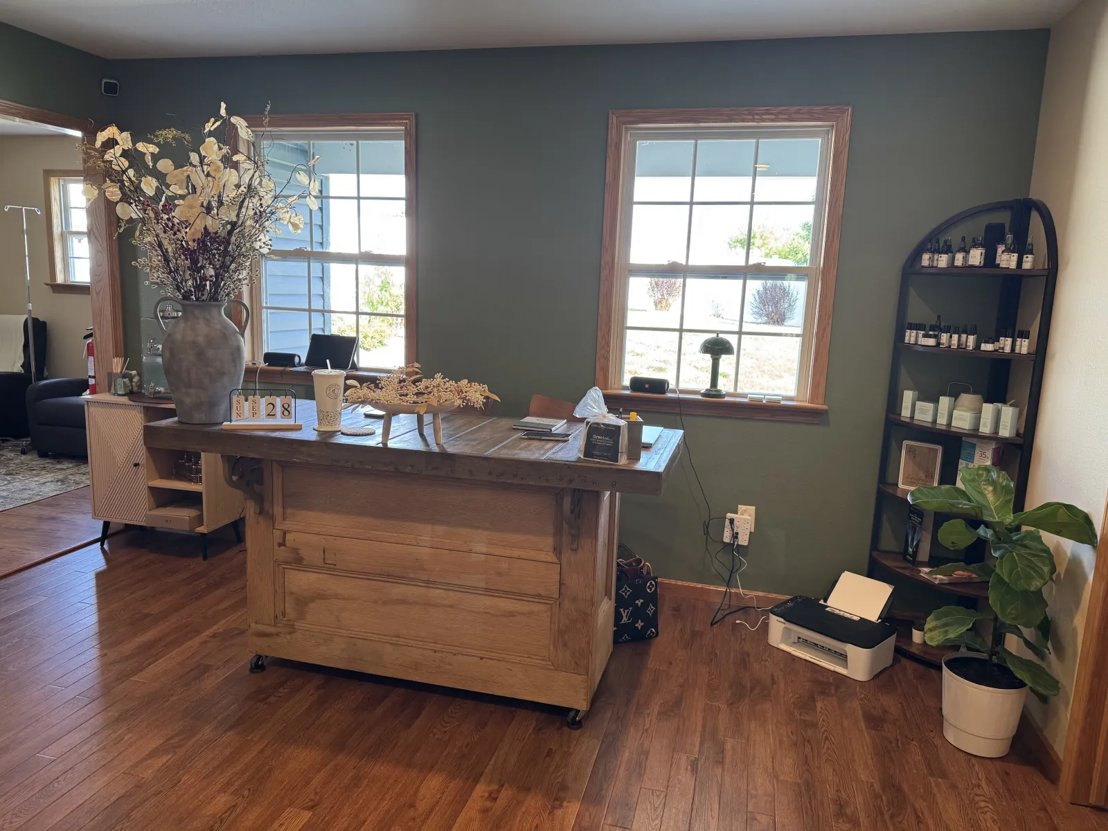 Reception desk with dried flowers, sage green walls, and a shelf of skincare products